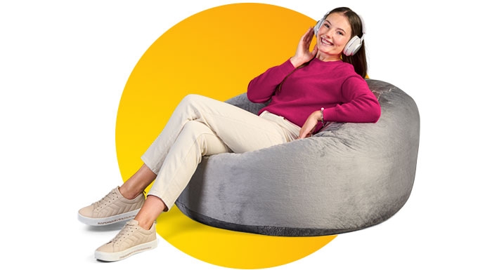 Portrait von Nikita, die entspannt auf einem grauen Sitzsack liegt und mit Kopfhörern Musik hört