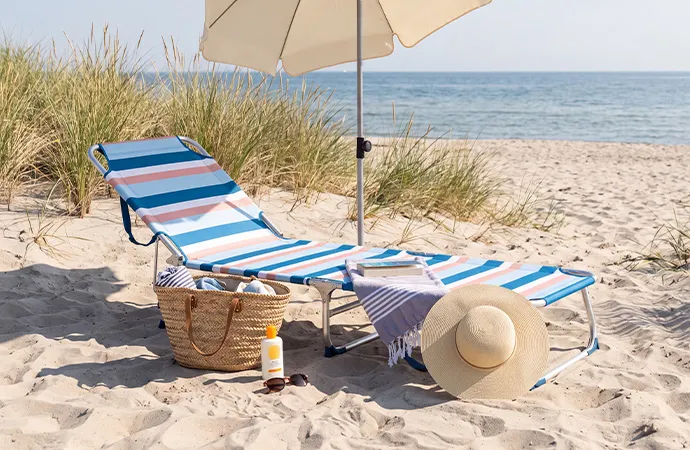 blau-weiß-rosa gestreifte Sonnenliege, beiger Sonnenschirm, Strandtasche, Sonnenhut, weitere Accessoires