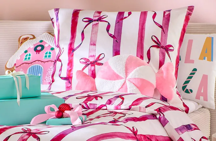 Weiße Bettwäsche mit pinken Schleifen, rosa Kissen in Hausform, rosa-weißes Kissen in Bonbon-Form, weißes Kissen mit buntem Lala-Aufdruck