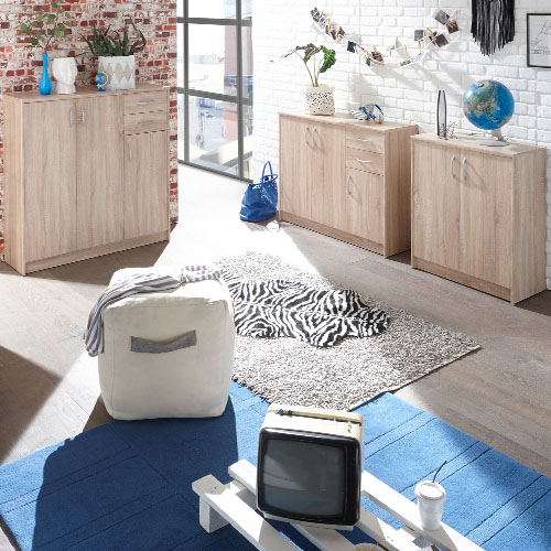 Kommoden unterschiedlicher Größe in Holzoptik, weißer Pouf, blauer und grauer Teppich, Fell in Zebra-Optik, Deko