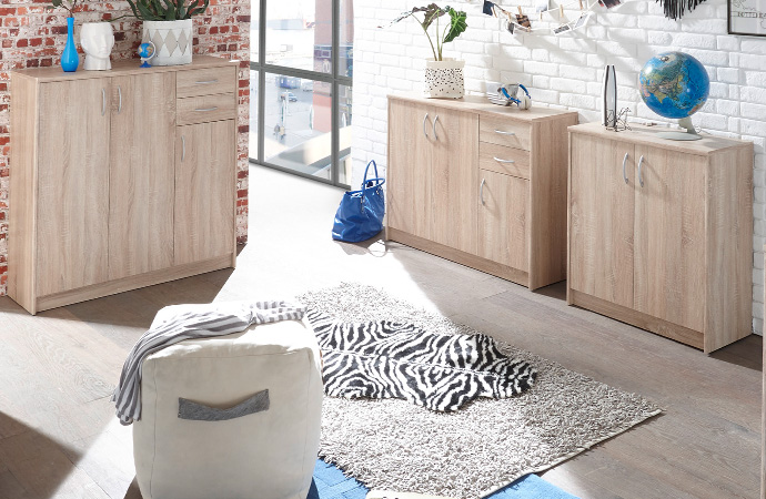 Kommoden unterschiedlicher Größe in Holzoptik, weißer Pouf, blauer und grauer Teppich, Fell in Zebra-Optik, Deko