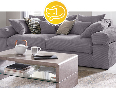 Wohnzimmer mit grauem Cordsofa und Couchtisch in Betonoptik mit Glasablage, Deko.