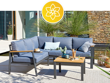 Terrasse mit Lounge-Ecksofa aus Metall mit grauen Auflagen und passendem Tisch aus Metall mit Tischplatte in Holzoptik.