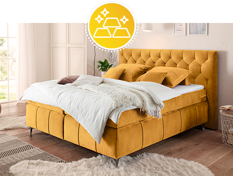 Goldgelbes Boxspringbett mit goldgelben Kissen, weißer Bettwäsche, weißer Decke in einem Schlafzimmer.