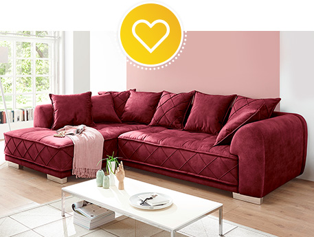Rotes Ecksofa mit vielen Kissen, rosa Decke, weißer Couchtisch, Deko.