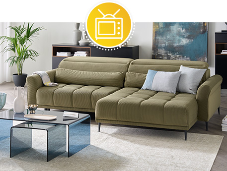 Wohnzimmer mit olivgrünem Cordsofa und farbigen Glastischen