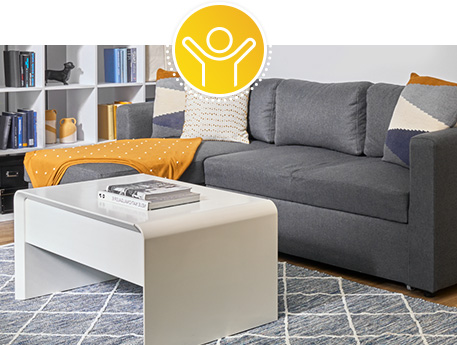 Single-Wohnung mit grauem Ecksofa, weißem Couchtisch, grau-weißem Teppich mit Rautenmuster, Raumteiler in Weiß mit Deko