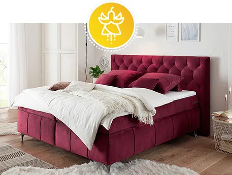 Bordeauxrotes Boxspringbett mit bordeauxroten Kissen, weißer Bettwäsche, weißer Decke und weißem Langflorteppich in einem Schlafzimmer